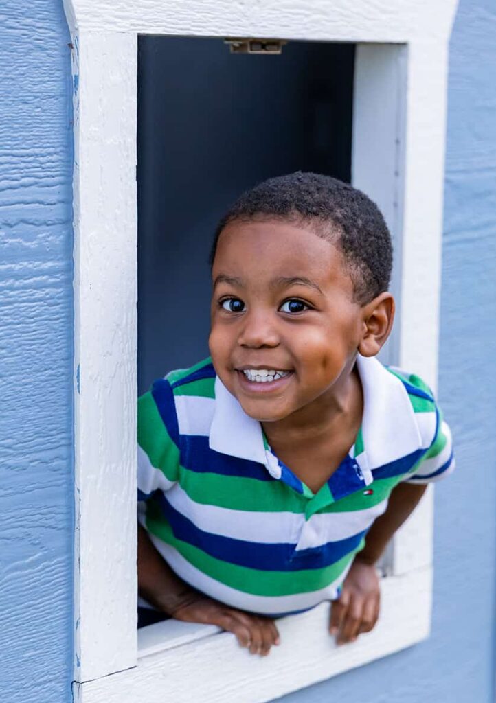photo of a smiling boy peering out of a playhouse window